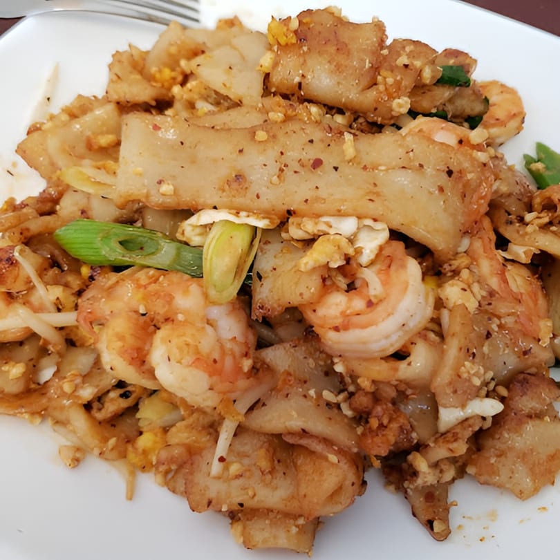 Close-up of Thai Pad See Ew with wide rice noodles, shrimp, egg, and green onions.